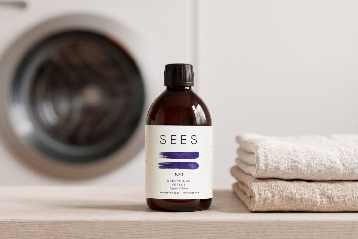 SEES Laundry Vinegar Bergamot & Lemon in an amber glass bottle on a laundry room shelf, folded linen towels beside it.